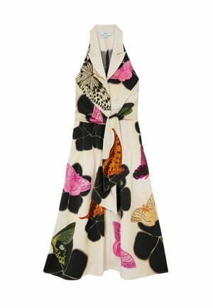 Frau mit langen Haaren in einem ärmellosen Kleid mit Kragen und großen Schmetterlings- sowie schwarzen Blumenmustern, die flache Sandalen trägt und an einer weißen Wand steht.