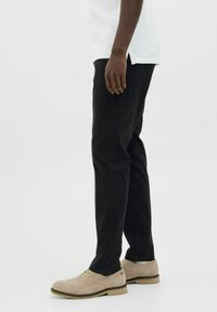 Zwarte broek met een slim fit, met een gladde textuur en subtiele details. Gecombineerd met licht tan suède schoenen.