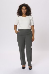 Top bianco aderente a maniche corte abbinato a pantaloni sartoriali verde scuro con tasche laterali. Il modello indossa tacchi neri a punta.