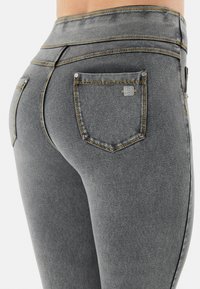 Harmaat korkeavyötäröiset farkut, joissa on sileä pinta, kaksi takataskua metallisilla yksityiskohdilla ja kontrastivärinen ommel.