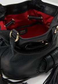 Sac seau en cuir noir avec un extérieur texturé, une doublure intérieure rouge, des accessoires en or et une fermeture à cordon. Présente des pompons sur le côté.