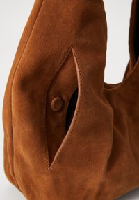 Brown suede handbag featuring a rounded shape, large opening, and an accented side with a visible button detail. Soft texture throughout.