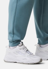 Weiße Sportsneakers mit strukturierten Overlays und Netzakzenten, kombiniert mit taillierten, hellblauen Jogginghosen mit Bündchen.