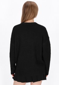 Pulover oversized negru din material moale, texturat, cu guler rotund și umeri căzuți. Dispune de o margine ribbed și o croială relaxată.