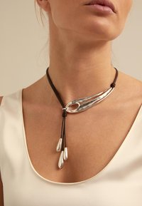 Collar de pendant de plata en un cordón de cuero marrón, con un diseño alargado y elegante que cuenta con dos acentos colgantes. Superficie suave y reflectante.