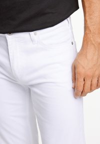 Weiße Jeanshose mit einer figurbetonten Passform, ausgestattet mit Vordertaschen und metallischen Hardware-Akzenten. Die Textur wirkt glatt und leicht dehnbar.
