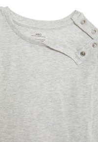 Graues Baumwoll-T-Shirt mit rundem Ausschnitt, ausgestattet mit einer diagonalen Knopfleiste mit drei Druckknöpfen an der linken Schulter. Weicher Stoff.