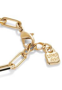 Pulsera de cadena de oro que presenta formas ovaladas y rectangulares interconectadas, un cierre de langosta y un pequeño charm con un candado grabado que dice "UNO de 50".