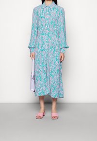 Robe à manches longues avec un imprimé abstrait bleu et rose ; dotée d'un avant à boutons et d'une coupe décontractée. Associée à des sandales à talons blocs roses et à un sac lilas.