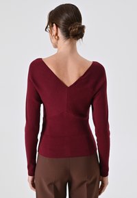 Maglione aderente bordeaux con retro a V, realizzato in tessuto morbido, con maniche lunghe e un design sartoriale per una silhouette snella.