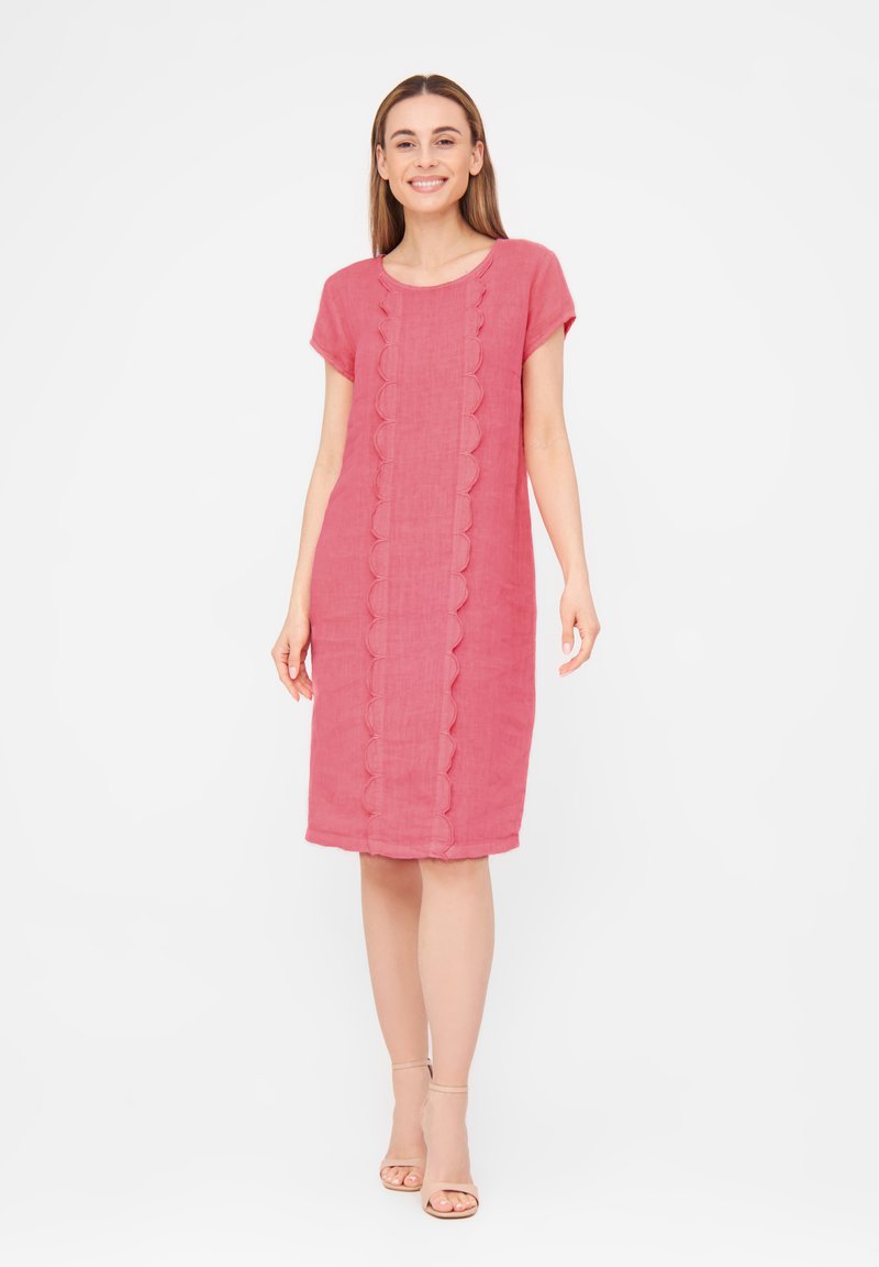 Robe en lin rose à manches courtes, avec un détail festonné au centre et une coupe ample. Texture lisse, longueur au genou, portée avec des sandales.