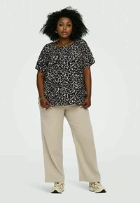 Top de mangas curtas com padrão de leopardo, feito de tecido suave, combinado com calças largas em bege. Modelo usa ténis. Design simples e descontraído.
