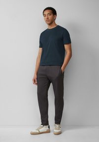 Marineblauwe katoenen t-shirt, grijze tapered broek en witte sneakers met gestructureerde zolen. Gladde stofafwerking en subtiele accenten aan de zijnaad.