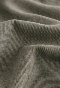 Grauer Stoff mit einer strukturierten Webart, der weiche Falten und subtile Farbnuancen zeigt. Das Material wirkt robust und eng gewebt.