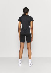 T-shirt de sport noire et shorts noirs, design ajusté, manches courtes, matériau doux, porté avec des chaussettes blanches et des chaussures de sport. Vue de dos.