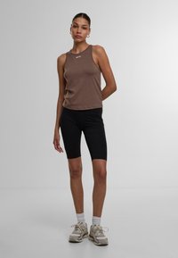 Brun ärmlös topp med rund halsringning, i kombination med svarta cykelbyxor. Outfiten har en slät textur och en kroppsnära design.