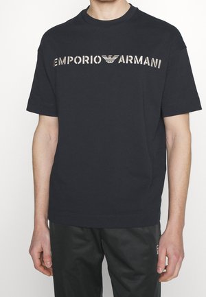 Czarna bawełniana koszulka z wyraźnym logo "EMPORIO ARMANI" w metalicznym srebrnym kolorze, wygodnym krojem z krótkimi rękawami i klasycznym okrągłym dekoltem.