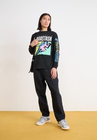 Black long-sleeve shirt featuring colorful graphic design and text on front and sleeves, paired with loose black pants and patterned sneakers.