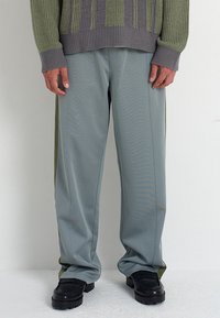 Ανοιχτό γκρι, ελαφρώς φαρδιά παντελόνια με σκούρους πράσινους κομψούς τόνους στο πλάι. Λείος υφή και διακριτική γυαλάδα, σε συνδυασμό με μαύρα υποδήματα.