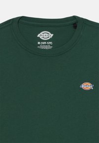 Green cotton t-shirt featuring a crew neck, short sleeves, and a small embroidered logo on the left chest area. Size M (10Y-12Y).