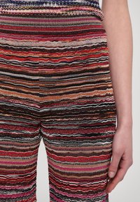 Pantaloni cu dungi multicolore, cu linii ondulate în roșu, roz, portocaliu și negru, confecționați dintr-un material texturat, cu o potrivire confortabilă.