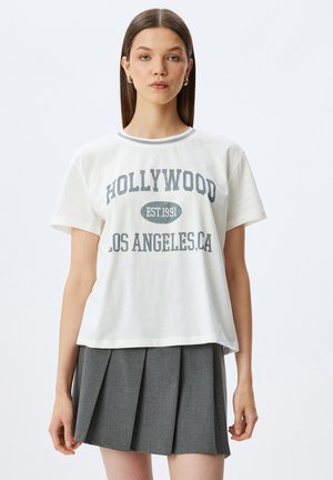 T-shirt en coton blanc avec le texte "HOLLYWOOD EST. 1991 LOS ANGELES, CA" en gris foncé. Encolure ronde avec bord contrastant. Coupe décontractée.