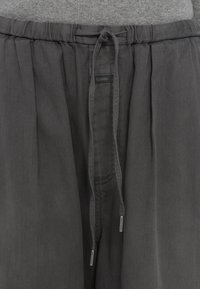 Pantalon gris foncé avec une taille élastique et un cordon de serrage noué, avec une petite étiquette de marque "Closed" au centre devant.