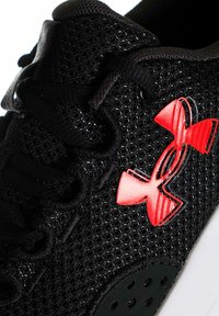 Scarpa sportiva nera con tomaia in mesh testurizzato, lacci neri piatti e un grande logo rosso Under Armour sul lato.