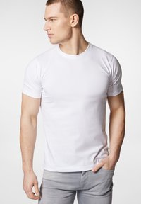 Biała bawełniana koszulka z okrągłym dekoltem, krótkimi rękawami i dopasowanym krojem. Noszona z jasnoszarymi dżinsami, o gładkiej fakturze.