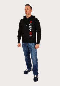 Hanorac negru cu fermoar, având logo-ul roșu și alb "USPA 90", dotat cu glugă, mâneci lungi și tiv bandat, asortat cu blugi și adidași.