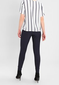 Bílý krátký rukáv top s vertikálními námořnickými pruhy, spárovaný s námořnickými pruhovanými legínami a černými botkami na podpatku. Minimalistický design a textura.