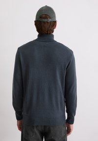 Pulover de culoare albastru închis cu guler înalt, manșete și tiv cu dungi. Purtați cu o pălărie gri, arătat din spate. Textură netedă, design pulover.