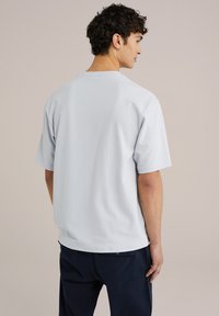 Svijetloplava pamučna majica sa kratkim rukavima i okruglom izrezom. Osim opuštenog kroja, ima jednostavan dizajn i prikazana je iz stražnjeg pogleda.