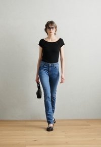 Top scurt negru cu mânecă scurtă, blugi din denim albastru deschis, geantă neagră și pantofi negri. Texturi fine și un design ajustat îmbunătățesc ținuta.