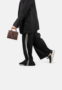Bolso de mano de estampado de leopardo con dos asas, combinado con una blazer negra oversized, pantalones anchos negros con rayas blancas laterales y zapatillas de deporte negras.