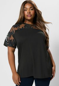Czarna bluzka z siateczkowymi rękawami z haftem kwiatowym, okrągły dekolt, miękka tkanina, luźny krój oraz kontrastowe tekstury.
