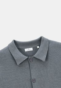 Polo gris en tissu texturé, avec un col, deux boutons foncés, et une étiquette indiquant "SERCE BLANCO" avec la taille "L."
