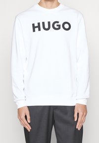 Sudadera blanca con un logo negro "HUGO" en el pecho. Fabricada en un material suave, tiene un cuello redondo y puños acanalados.