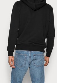 Felpa nera con cappuccio dal tessuto morbido e polsini a costine, abbinata a jeans in denim azzurro chiaro con tasche posteriori e un finish slavato.