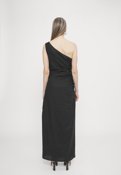 Black one-shoulder dress in a long, fitted design. Features textured fabric with a side ruched detail and high-heeled shoes.