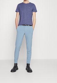 Kurzarm, runder Hals lila T-Shirt kombiniert mit hellblauen Slim-Fit-Hosen, schwarzem Gürtel und schwarzen Stiefeletten mit dicker Sohle.