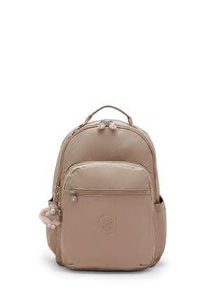 Sac à dos beige avec poche zippée à l'avant, poignée de transport, poches latérales et petit porte-clés en peluche attaché à la tirette de la fermeture éclair côté gauche.