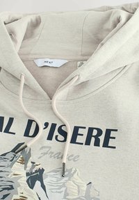 Beżowa bluza z kapturem ze sznurkiem i srebrnymi końcówkami. Posiada grafikę gór oraz napis "Val D'Isere Francja" w granatowym kolorze. Miękka tekstura.