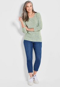 Grüner und blauer strukturierter Strickpullover mit Dreiviertelärmel, kombiniert mit blauen knöchellangen Jeans und weißen Sneakern.