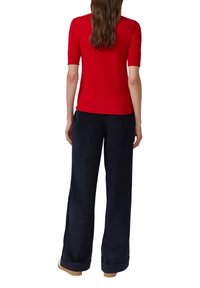 Czerwony krótki rękaw sweter zestawiony z granatowymi spodniami o szerokiej nogawce, charakteryzującymi się gładką fakturą i kontrastującymi kolorami. Luźny krój i prosty design.
