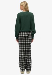 Grüner übergroßer Pullover mit einem quadratischen Aufnäher, kombiniert mit schwarz-weiß karierten, weit geschnittenen Hosen. Strukturierter Stoff und lässige Passform.