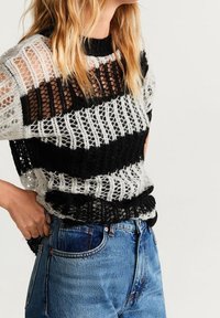 Top in maglia con motivo a righe bianche e nere, tessuto a trama aperta, maniche corte e scollatura rotonda, abbinato a jeans blu a vita alta.