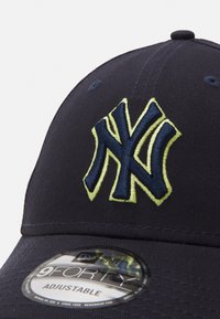 Gorra de béisbol ajustable en azul marino con el logotipo "NY" bordado en amarillo y azul oscuro. Presenta una tela texturizada y una etiqueta New Era 9FORTY.
