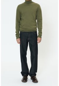 Pull à col roulé côtelé vert olive assorti à un jean en denim foncé ample et des mocassins marron brillants avec des accents décoratifs.