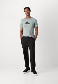 Lichtgroen katoenen T-shirt met zwart "ANTONY MORATO" logo, gecombineerd met zwarte broeken en zwarte sneakers met witte zolen. Casual pasvorm.